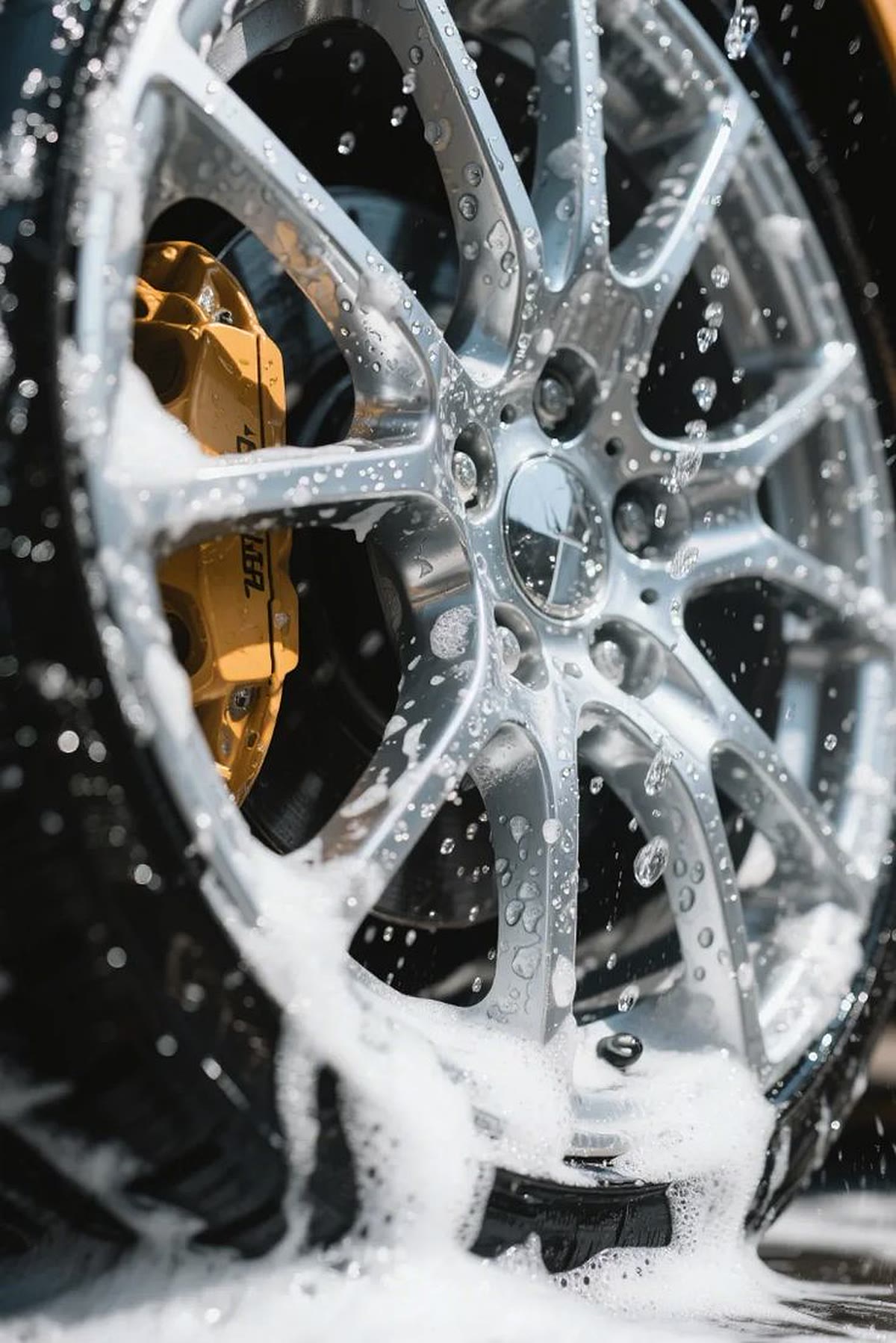 Alloy wheel covered in foam and water droplets during a wash